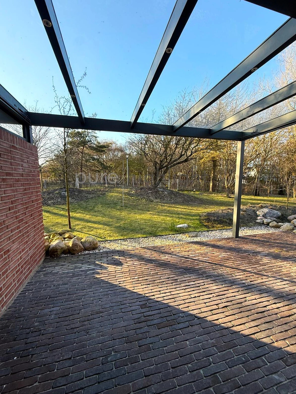 Gepflasterte Terrasse unter Glasdach mit Blick in den Garten